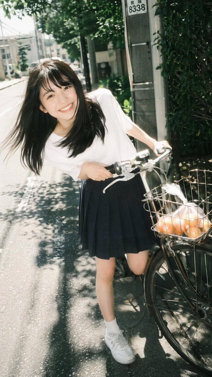A vintage film photography portrait of a young Asian woman smiling broadly at the camera. She is leaning forward playfully while holding the handlebars of a bicycle on a sunny neighborhoo...